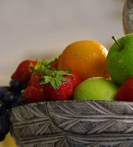 Close-up of assorted fresh fruits like apples, oranges, and strawberries in a ceramic bowl.